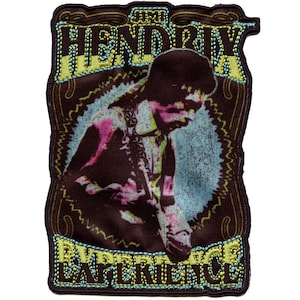 Könnte beinhalten: Ein brauner Stoff-Patch mit gelber und blauer Stickerei. Der Patch zeigt ein Porträt von Jimi Hendrix, der Gitarre spielt, mit dem Text "The Jimi Hendrix Experience" in gelber und blauer Stickerei.
