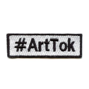 May include: Black and white embroidered patch with the text "#ArtTok" on a white background.