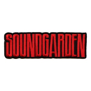 May include: Embroidered patch with the word "SOUNDGARDEN" in red capital letters. The text is stitched onto a black rectangular background. The patch is designed to be ironed or sewn onto clothing or accessories, a common item for music fans.