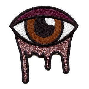May include: Embroidered iron-on patch of a brown eye with a white sclera and a burgundy eyelid. The eye is dripping with pink glitter.