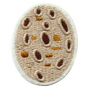 Puede incluir: Un parche redondo bordado de color beige con formas ovaladas marrones y doradas.