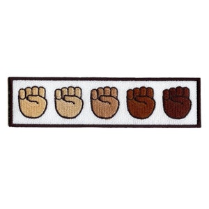 Pode incluir: Cinco punhos levantados em fila, cada um de um tom de marrom diferente, do claro ao escuro. Os punhos são bordados em um fundo branco com uma borda marrom.