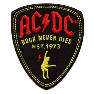 May include: Black and yellow embroidered patch with the text "AC/DC Rock Never Dies Est. 1973" and a yellow silhouette of a person playing guitar.
