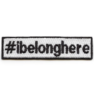 Puede incluir: Parche blanco bordado con costuras negras. El parche dice "#ibelonghere" en una fuente en negrita, sans-serif.