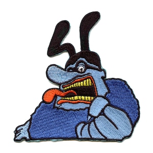 May include: Embroidered patch featuring a blue, cartoon monster with a large, open mouth, a long, red tongue, and black ears. The monster is wearing a black hat and has a white eye.