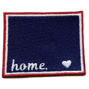 Puede incluir: Parche bordado blanco con fondo azul y borde rojo y blanco. El parche dice "home" con un corazón blanco.