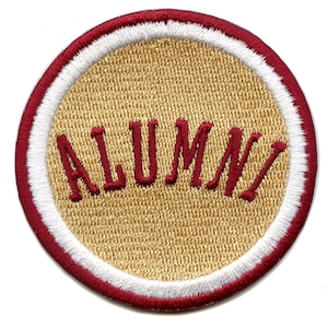 Puede incluir: Un parche redondo bordado en color dorado con un borde blanco y un borde rojo. El parche dice "ALUMNI" en rojo.