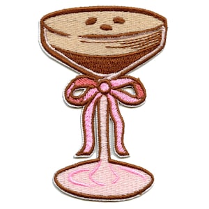 Pode incluir: Etiqueta bordada para passar a ferro de um copo de champanhe castanho com um laço rosa.