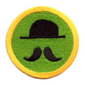 May include: A green and yellow embroidered patch with a black bowler hat and mustache.