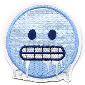 May include: A blue and white embroidered patch of a frozen face with a dripping mouth. The face is a cartoon style with a simple design.