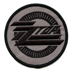 May include: A gray and black embroidered patch with the word "ZZ Top" in a stylized font.