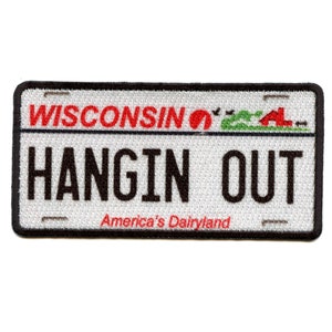 May include: Embroidered patch in the shape of a Wisconsin license plate. The patch features the word "WISCONSIN" in red, the words "HANGIN OUT" in black, and the phrase "America's Dairyland" in red. The patch has a black border.
