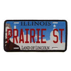 Op de afbeelding: Een blauw en wit Illinois kenteken met de tekst "PRAIRIE ST" in rode letters en "LAND OF LINCOLN" in zwarte letters.