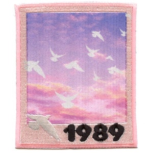 Puede incluir: Un parche bordado de color rosa y morado con una foto de una puesta de sol y pájaros blancos volando en el cielo. El año 1989 está bordado en negro en la parte inferior del parche.