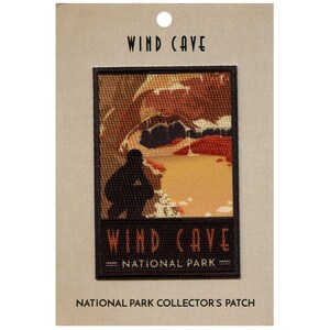 May include: A brown and black embroidered patch with the text "Wind Cave National Park" and a depiction of a cave entrance with a person standing in front of it.