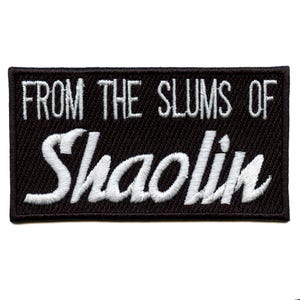Puede incluir: Parche rectangular negro con texto bordado blanco: "FROM THE SLUMS OF Shaolin". El parche tiene un borde negro y es probablemente un parche para planchar o coser para ropa o accesorios.