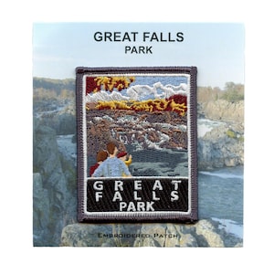 May include: Embroidered patch featuring a scenic view of Great Falls Park. The patch has a rectangular shape with a gray border and includes the park's name in white lettering. The image depicts a landscape with people, trees, and water.