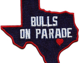May include: An embroidered patch in the shape of the state of Texas with a red outline. The patch is navy blue with white text that reads "BULLS ON PARADE" and a small red heart.