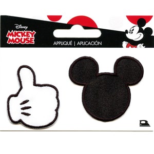 May include: Two iron-on patches featuring Mickey Mouse. One patch is a white silhouette of Mickey Mouse's hand giving a thumbs up. The other patch is a black silhouette of Mickey Mouse's head with large ears. The patches are packaged on a white card with the words "Disney Mickey Mouse" and "Appliqué | Aplicación".