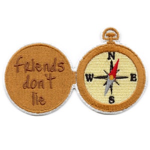 Peut inclure: Un compas brun et or avec un contour blanc. Le compas est ouvert et l'intérieur dit "Friends don't lie".