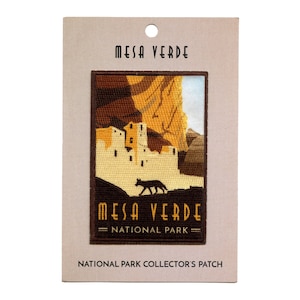 May include: A brown and tan embroidered patch with a depiction of Mesa Verde National Park. The patch features a cliff dwelling and a coyote walking in the foreground. The text "Mesa Verde National Park" is embroidered in brown on the patch.