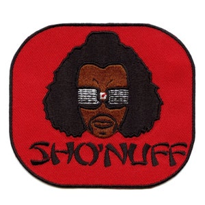Peut inclure: Patch brodé rouge avec une image de dessin animé d'une personne aux cheveux noirs, des lunettes de soleil et un visage brun. Le texte "SHON'NUFF" est sous l'image.