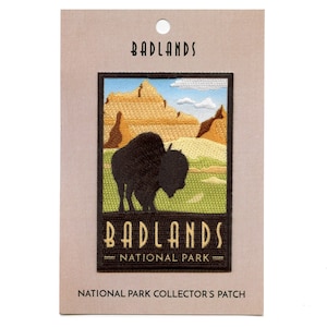 May include: A brown and green embroidered patch featuring a silhouette of a bison in front of a landscape. The patch reads "Badlands National Park" in yellow text.