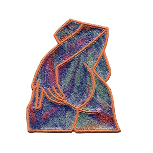May include: An embroidered patch with a holographic iridescent blue, purple, and pink design. The patch is outlined in orange thread and depicts a stylized human figure.