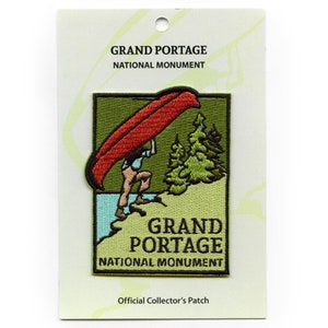 May include: A green, red, and brown embroidered patch with a person carrying a canoe. The patch says "Grand Portage National Monument" and "Official Collector's Patch".