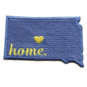 May include: A blue embroidered patch in the shape of the state of South Dakota with the word "home" and a yellow heart.