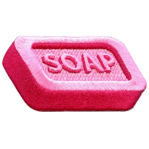 Peut inclure: Un patch brodé rose en forme de savon avec le mot "SOAP" en broderie blanche.