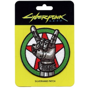 Może przedstawiać: Naszywka haftowana w kolorze zielonym, białym i czerwonym z srebrną, roboto-ręką wykonującą gest rock and roll. Naszywka zawiera napis "Cyberpunk 2077" i "Silverhand Patch".