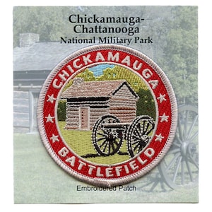 May include: Embroidered patch with a red border and white stars. The centre of the patch features a beige cabin with a brown door and a black cannon in front of it. The text "Chickamauga Battlefield" is in white lettering around the edge of the patch.