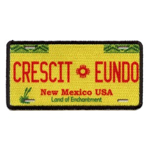 Op de afbeelding: Gele en groene geborduurde patch met de tekst "CRESCIT EUNDO" in rood, "New Mexico USA" en "Land of Enchantment" in zwart.