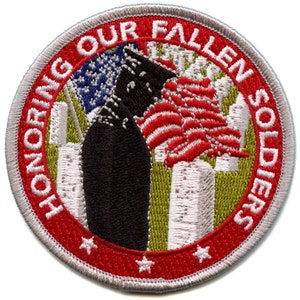 May include: A red, white, and blue embroidered patch with a silhouette of a soldier standing at attention in front of the Twin Towers. The text "Honoring Our Fallen Soldiers" is written around the edge of the patch.