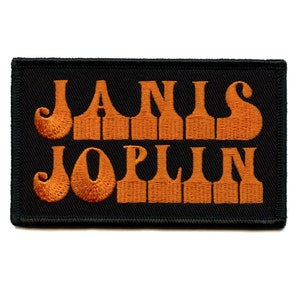 Puede incluir: Un parche bordado de color naranja con el texto "JANIS JOPLIN" sobre un fondo negro.