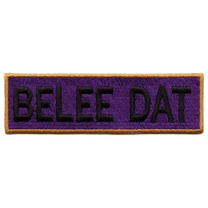 May include: Purple and gold embroidered patch with the text "BELEE DAT" in black.