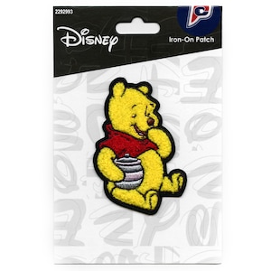 May include: Iron-on patch featuring Winnie the Pooh, a yellow bear, holding a honey pot. The patch is on a white background with black text that says "Disney" and "Iron-On Patch".