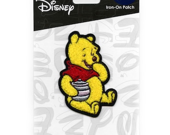 May include: Iron-on patch featuring Winnie the Pooh, a yellow bear, holding a honey pot. The patch is on a white background with black text that says "Disney" and "Iron-On Patch".