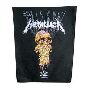 Pode incluir: Patch de tecido preto com o nome da banda "Metallica" em letras brancas. Um gráfico de uma caveira envolta em bandagens com um cérebro rosa está no centro. O texto "One" está na parte inferior do patch.