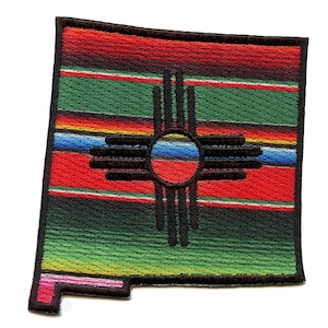 May include: A colourful embroidered patch shaped like the state of New Mexico. The patch features the state symbol, the Zia symbol, in black against a background of red, green, yellow, blue and white stripes.