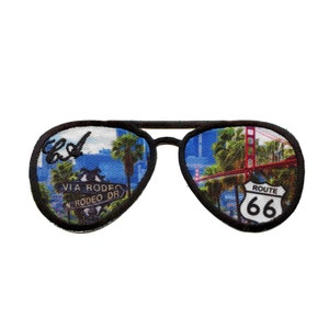 Könnte beinhalten: Ein gestickter Patch in Schwarzweiß von einer Aviator-Sonnenbrille mit Blick auf die Golden Gate Bridge und ein Route 66-Schild im rechten Glas und Blick auf den Rodeo Drive in Los Angeles im linken Glas.