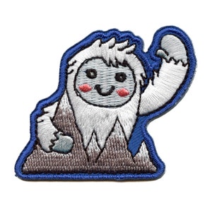 May include: Embroidered patch of a white yeti with a blue outline, standing on a gray mountain with a happy expression. The yeti has a white beard and is wearing a blue scarf.