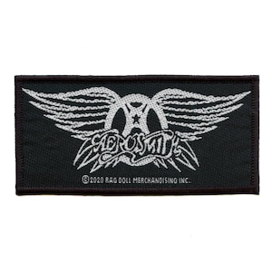 Könnte beinhalten: Ein gestickter Patch in Schwarz und Weiß mit dem Aerosmith-Logo mit Flügeln. Der Text "©2020 RAG DOLL MERCHANDISING INC." befindet sich am unteren Rand des Patches.