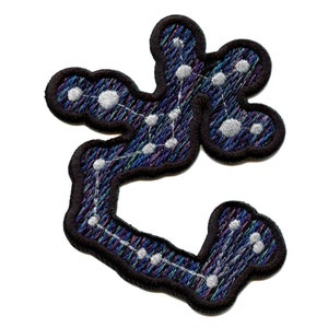 Può includere: Una toppa ricamata nera con un designo di costellazione in bianco e blu. La costellazione è delineata in nero e ha uno sfondo blu scuro.