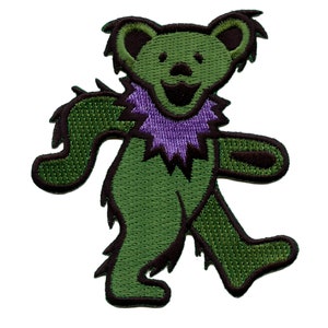 Puede incluir: Parche bordado verde de un oso bailando con una flor morada alrededor del cuello.