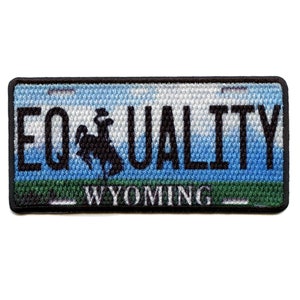 Op de afbeelding: Een geborduurde patch in zwart en wit met een blauwe, witte en groene achtergrond. De patch toont een silhouet van een cowboy die een paard berijdt met de tekst "EQUALITY" en "WYOMING" eronder.