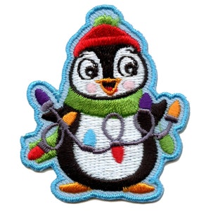May include: A cartoon penguin wearing a red hat and green scarf is holding a string of colorful Christmas lights. The penguin is embroidered on a blue background.