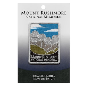 Könnte beinhalten: Bügeleisen-Aufnäher mit einem weißen gestickten Bild des Mount Rushmore National Memorial mit blauem Himmel und weißen Wolken. Der Aufnäher ist weiß mit schwarzem Text, der "Mount Rushmore National Memorial" und "Traveler Series Iron-on Patch" lautet.