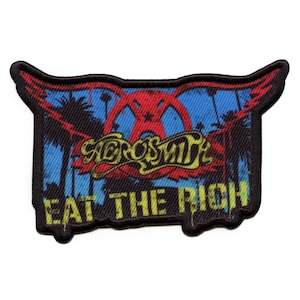 Könnte beinhalten: Ein schwarzer und gelber gestickter Patch mit den Worten "Aerosmith" und "Eat the Rich" in einer stilisierten Schrift. Der Patch zeigt eine rote und gelbe Grafik eines geflügelten Symbols mit Palmen im Hintergrund.